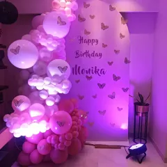 A lovely pink and purple butterfly-themed decoration. An arched backdrop is adorned with butterfly stickers and a cascading balloon garland, all illuminated by soft purple lighting.