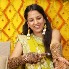 Your big day, our little touch of magic. A happy bride pointing to her intricate mehndi design, filled with personal stories.