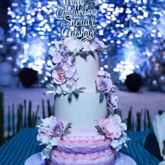 The 25th-anniversary cake in its element, set against a sparkling blue backdrop at the celebration. The silver "Happy 25th Anniversary" topper adds the final touch.