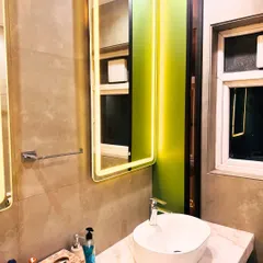 A closer look at the single vanity setup, showing the elegant combination of the white sink, marble top, and lime green accent wall. The backlit mirror provides perfect task lighting.