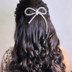 A chic and modern half-updo. The voluminous curls are gathered with a sparkling bow accessory, perfect for an engagement, reception, or cocktail party.