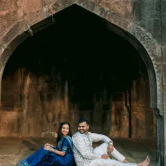 Framed by a stone archway, Ankush and Aishwarya share a relaxed moment. The contrast between her vibrant blue saree and the rustic stone creates a visually stunning pre-wedding portrait.