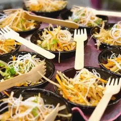 Individual portions of a refreshing glass noodle salad, served with eco-friendly wooden forks. We are committed to thoughtful presentation and sustainability.