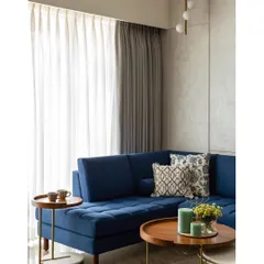 Another angle of the living room, showing the tufted blue sofa and nested coffee tables. The design proves that using a strong, solid color can create a joyful and elegant space.