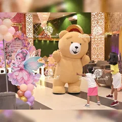 Kids love meeting their favorite characters. Here, a giant teddy bear mascot gives hugs and takes photos with the young guests at a fairy-themed party.