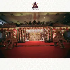 A classic South Indian temple-style mandap, complete with carved elephants and traditional floral arrangements. The red carpet and rich textures create a regal and sacred atmosphere for the wedding rites.