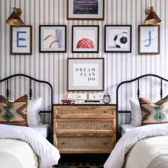 This bedroom was designed for two boys, blending the home's Spanish theme with fun, personal touches. The twin black metal beds are separated by a rattan chest of drawers, set against a striped wallpaper and a gallery wall of sports and motivational art.