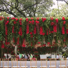 A grand canopy of hanging red florals and lush greens creates a stunning dining experience. This overhead installation defines the space and immerses guests in a romantic, garden-like atmosphere.