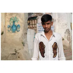 A young man in a shirt adorned with angel wings, shot against a rustic wall in Delhi. The juxtaposition of modern fashion and the old, textured background creates a compelling street portrait.