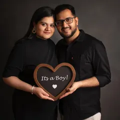 A smiling couple holds a heart-shaped sign to announce they are expecting a baby boy. A classic and joyful announcement portrait.