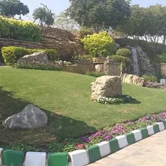 A roadside beautification project featuring a sloping lawn, rock formations, and a small waterfall. This shows how we turn unused public land into attractive green spots.