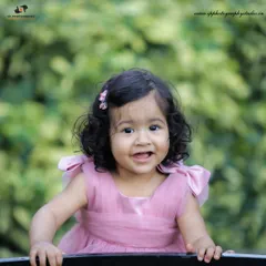 This outdoor portrait of a toddler in a lovely pink dress captures her bright smile and cheerful personality against a natural green background.