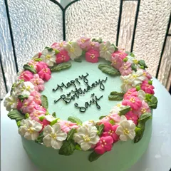 A side view of the floral wreath birthday cake. This angle highlights the height and dimension of the buttercream flowers and the smooth finish on the sides of the cake.