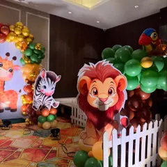 Our jungle theme is filled with friendly faces. This corner of the party features adorable cutouts of a lion, zebra, and a parrot perched on a balloon tree, all behind a classic white picket fence.