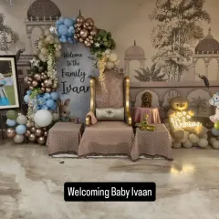 A grand and royal-themed 'Welcome Home' party for baby Ivaan. This setup features a beautiful throne, a custom backdrop, and an elaborate balloon arch in a sophisticated color palette of blue, green, and bronze.