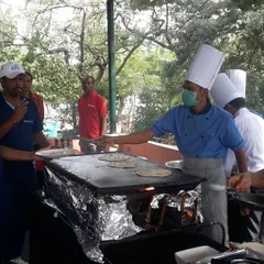 A chef serving a freshly made dosa from a live counter at an outdoor event. Live stations like these are a great way to offer hot, customized food and entertain guests at the same time.