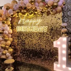 A first birthday party with a touch of glamour. The gold sequin wall provides a sparkling background for the peach and gold balloon arch and the light-up number '1'.