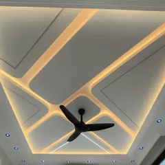 A stunning example of a modern false ceiling design. The geometric pattern with integrated LED strip lighting creates a dynamic and futuristic look, transforming the ceiling into a major design element.