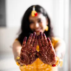 A creative Haldi shot focusing on the bride's intricate mehendi. Her joyful, blurred smile in the background adds context, but the beautiful henna design is the star of this photo.