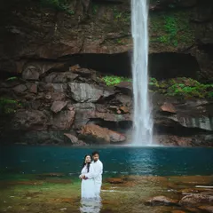 An intimate moment in the shallows of a turquoise pool, with the waterfall as a stunning backdrop. This candid wedding photography style focuses on the couple's connection amidst nature's grandeur.