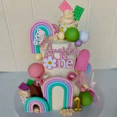 A whimsical candy-themed masterpiece for a first birthday. This 3kg cake is bursting with color, featuring pastel rainbows, candy spheres, butterflies, and mini cupcakes, with chocolate truffle and vanilla mixed berries flavors.