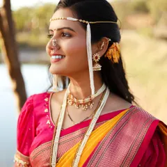 A joyful outdoor portrait of a bride in a traditional Maharashtrian Paithani saree. The natural light and green background make the bright yellow and pink of the saree stand out.