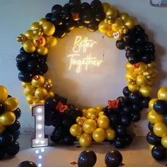 This first-anniversary decoration features a stylish black and gold theme. The balloon ring is complemented by a "Better Together" neon sign and an illuminated marquee number '1', creating a chic and modern look.