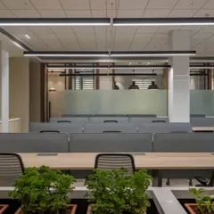 A view of the clean and organized workstation setup. The neutral color palette of the desks and dividers is complemented by the vibrant green of the plants, creating a balanced and calming workspace.