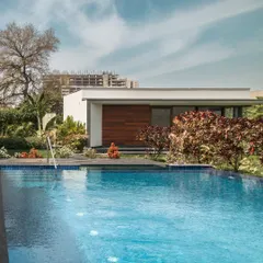 The pool at Rosewood Farmhouse is designed for tranquility. Its calm blue water reflects the sky and the clean lines of the adjacent pool house, while colorful croton plants add a vibrant splash of color to the serene setting.