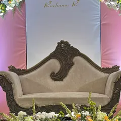 An elegant carved sofa set against a simple backdrop, surrounded by fresh floral arrangements, perfect for a sophisticated engagement or naming ceremony.