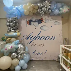 A clear photo of the airplane-themed first birthday backdrop for Ayhaan. The soft color palette and watercolor-style graphics create a gentle and charming atmosphere for a baby's first big celebration.