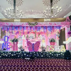 A grand stage setup for a butterfly-themed first birthday, with a canopy of hanging flowers and balloons, and large light-up butterfly props.