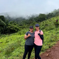 Enjoying the view of the misty, forest-covered hills from the Bandaje trek trail. The landscape is a stunning mix of green meadows and dense shola forests.