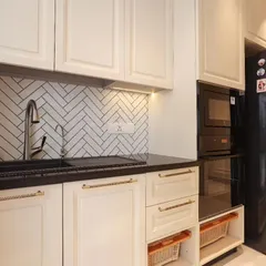 This shot highlights the functional aspects of a classic kitchen design, including an integrated oven and microwave tower, a deep sink, and open wicker basket drawers for vegetable storage.
