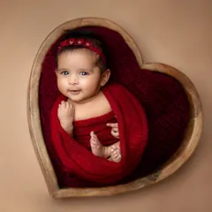 A beautiful baby girl wrapped in red, smiling softly in her sleep. The neutral background makes the rich color and her expression pop.