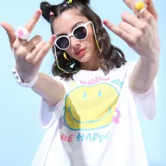 A close-up of the 'Be Happy' oversized tee. The styling is fun and approachable, with quirky rings and sunglasses to appeal to a young, trend-conscious audience.