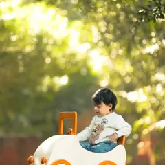 A wider view of the "tiny adventurer" in his toy car, set against a backdrop of lush green trees with beautiful bokeh. This lifestyle shot captures a quiet moment of play in a natural setting.
