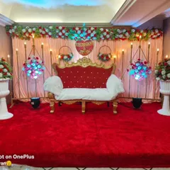 This engagement stage features a vibrant red theme with a custom heart sign for the couple, Khushboo and Jitesh. The setup includes a plush red carpet, a royal red and white sofa, and uplighting that makes the floral arrangements stand out.