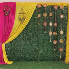 A vibrant Mehendi backdrop combining a grass wall with pink and yellow drapes. We added traditional hangings and marigold borders to complete the festive look.