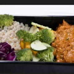 A close-up of one of our meal prep containers, showing a balanced portion of brown rice, steamed broccoli, and a flavorful curry. This is a typical example of how we structure our meals to meet your protein requirements.