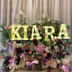 Celebrating a birthday should be as unique as the person themselves. This stunning floral hamper, personalized with the name 'Kiara' in glowing marquee letters, is designed to be an unforgettable centerpiece for any celebration.