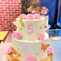 A beautiful two-tier white cake adorned with pink buttercream roses and delicate edible butterflies. This is a classic and elegant choice for a 5th birthday.
