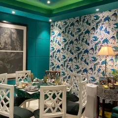 We love to embrace bold design choices that reflect our client's personality. This eclectic dining room features a dramatic teal wall and a vibrant, bird-patterned wallpaper, creating a rich and immersive experience. The custom malachite stone tabletop and hand-carved white chairs serve as statement pieces, making every meal an occasion.