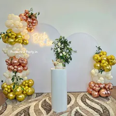 For a modern and chic bridal shower, we offer this elegant setup. It features clean white arched backdrops, a stylish "Bride to be" neon sign, and sophisticated balloon columns in cream, gold, and rose gold, accented with fresh greenery.