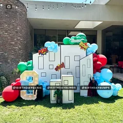 An outdoor superhero setup with building-shaped backdrops, "POW" and "BOOM" comic book effects, and character props of the Hulk and Superman.