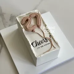 A chic rectangular cake for a 27th birthday. The design features trendy balloon-style numbers and a "Cheers" message.