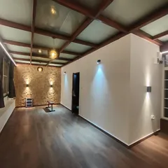 A view of a completed media room with a glass and wood-beamed pergola roof. The structure allows for ample natural light while providing shelter, and the interior is finished with warm wood flooring and modern lighting.