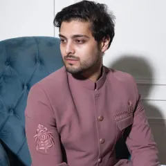 A seated portrait displaying the elegant drape of the pink Prince Coat. The tonal Resham embroidery on the sleeve adds a layer of sophisticated detail without overwhelming the look.