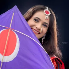 A playful portrait where the woman peeks out from behind a purple kite, or *patang*. This shot captures the fun and festive spirit of the Makarsankranti festival.