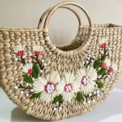 This lovely beach bag, made from woven natural fibers, features delicate white and pink floral embroidery. It's a perfect accessory for a summer outing or a thoughtful, handcrafted gift.